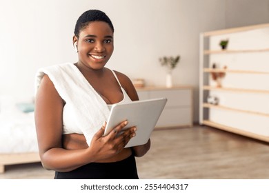 Online weight loss workout. Plump black lady with tablet pc watching sports video tutorial at home. Plus size African American woman with touch pad communicating with personal trainer on web - Powered by Shutterstock