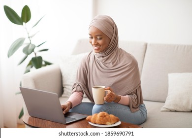 Online Work, Education, Communication Concept. Happy Black Lady In Hijab Using Laptop And Drinking Coffee At Home. Positive Muslim College Teacher In Headscarf Giving Lesson On PC Webcam