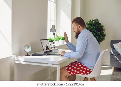 Online work at home. Funny man in red shorts works communicates using laptop sitting at the table at the workplace at home office in the room.
