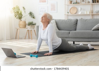 Online Yoga Lessons. Fit Senior Woman Standing In Cobra Pose In Front Of Laptop At Home, Enjoying Healthy Lifestyle, Free Space