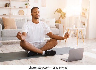Online Yoga. Relaxed African American Man Meditating At Laptop Sitting In Lotus Position Relaxing At Home With Eyes Closed. Everyday Meditation And Relaxation, Keep Calm Concept. Selective Focus