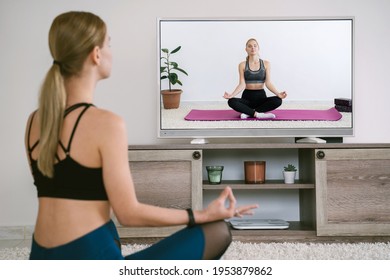 Online Yoga Training At Home Concept. Woman Doing Meditation And Watching Video Streaming On TV Screen. Distance Sport At The Quarantine Time.