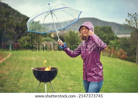 Only the brave barbeque in the rain. Shot of a woman holiding an umbrella while trying to barbeque in the rain.
