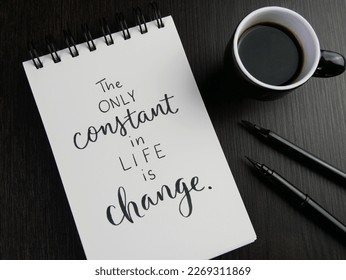 THE ONLY CONSTANT IN LIFE IS CHANGE lettering in notebook with cup of coffee and pens on black wooden desk