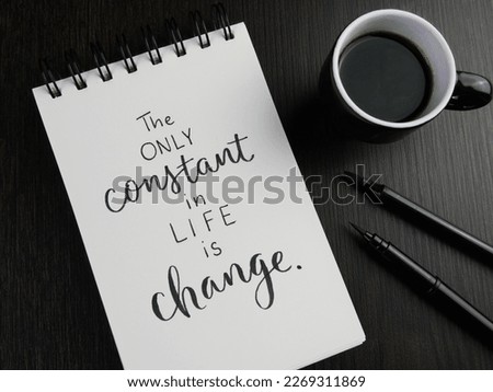 THE ONLY CONSTANT IN LIFE IS CHANGE lettering in notebook with cup of coffee and pens on black wooden desk