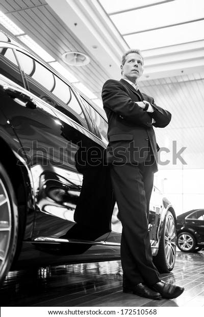 Only luxury cars. Black and white image of full\
length confident grey hair man in formalwear leaning at the car and\
looking away