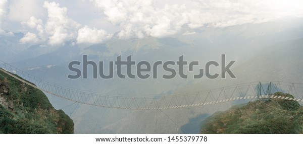 The\
only way in the mountains lit by sunlight. Empty suspension bridge\
high in the mountains on the background of\
clouds.