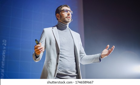 On-Stage Handsome Speaker Greets Audience, Talks About His Ideas, Concepts And New Age Product, In Background Screen Animation. Live Entrepreneurship Event  Start-up Conference  Device Presentation