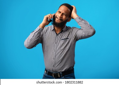 Oops, Bad News. Confused African Man Talking On Cell Phone, Having Problems, Grabbing His Head On Blue Wall