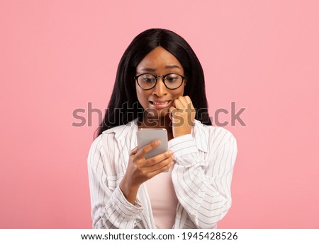 Oops. Embarassed black woman looking at mobile phone screen in confusion on pink studio background. Emotional African American lady making mistake while working in web