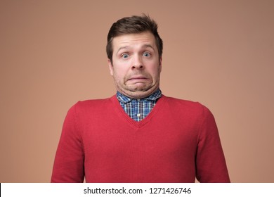 Oops. Funny Caucasian Man In Red Sweater Grimacing Guilty Face At Studio Background