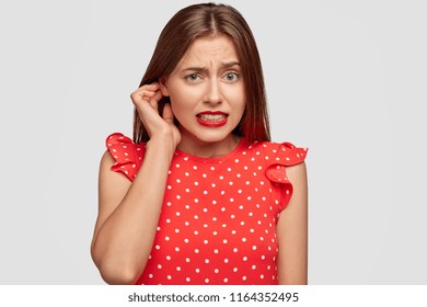 Oops! Good looking young European female feels embarrassed of awkward situation, clenches teeth, looks guilty, realises she has some problems, wears red lipstick and polka dot fashionable dress