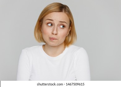 Oops, How Awkward! Close Up Studio Portrait Of Shy Awkward Young Woman Biting Lips Feeling Embarrassed, Confused And Nervous, Looking Aside, Isolated On Grey Background.