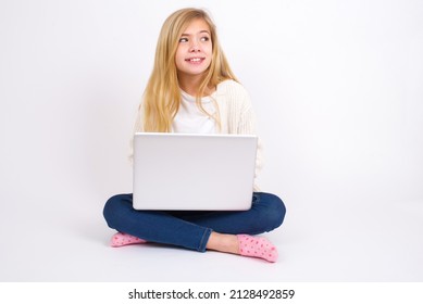 Oops! Portrait Of Beautiful Caucasian Teen Girl Sitting With Laptop In Lotus Position On White Background Clenches Teeth And Looks Confusedly Aside, Realizes Her Bad Mistake,