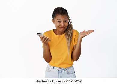 Oops. Smiling Cute Black Girl Shrugging Shoulders And Looking With Sorry Face Expression, Clueless Of Something, Standing Over White Background