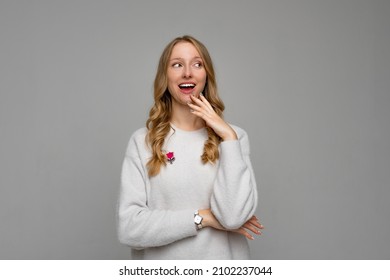 Oops sorry. Cute young blonde woman wearing cozy white sweater shrugging shoulders and cover his smile with palm coquettish, being coy while apologizing, gray background