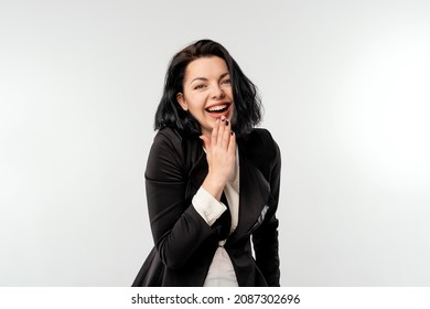 Oops sorry. Cute young businesswoman in black formal jacket white shirt shrugging shoulders and cover her smile with palm coquettish, being coy while apologizing, white background