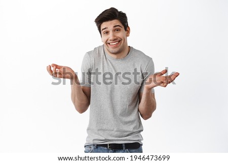 Oops sorry, my mistake. Man shrugging and smiling awkward, feeling guilty, apologizing and looking coy at camera, standing over white background