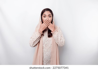 Oops! Surprised young Asian Muslim woman covering mouth with hands and staring at camera while standing against white background - Powered by Shutterstock