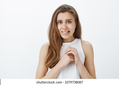 Oops, very awkward situation. Portrait of emberrassed good-looking european woman, rubbing hands over chest and grimacing, feeling ashamed and guilty, feeling anxious and nervous over gray wall