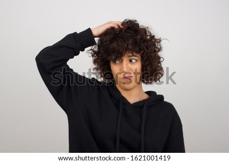 Oops, what did I do? Beautiful blonde woman holding hand on head with frightened and regret expression. Wearing casual clothes standing against gray background.