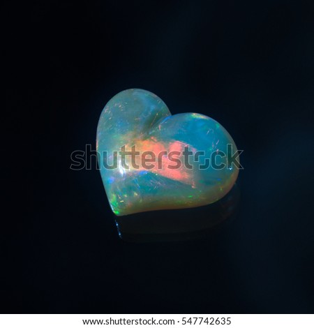 Opal jewelry cut, carved into the shape of a heart on a black background.
