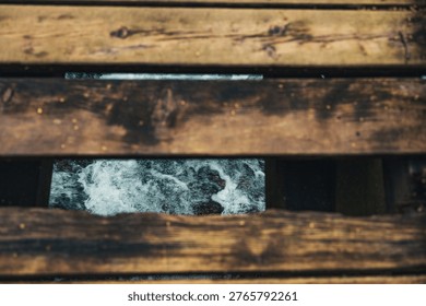op-down view through the gaps of a broken rustic wooden bridge showing rushing river water below in Ayazma, Bayramiç.