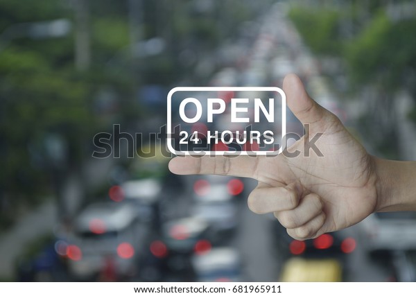 Open 24 hours icon on finger over blur\
of rush hour with cars and road, e-business\
concept