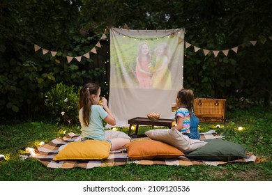 Open Air Cinema. Backyard Family Outdoor Movie Night With Kids. Sisters Spending Time Together And Watching Cimema At Backyard. DIY Screen With Film. Summer Outdoor Weekend Activities With Children.