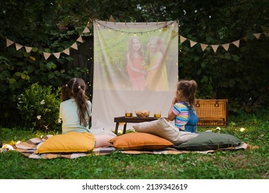 Open Air Cinema. Backyard Family Outdoor Movie Night With Kids. Sisters Spending Time Together And Watching Cimema At Backyard. DIY Screen With Film. Summer Outdoor Weekend Activities With Children.