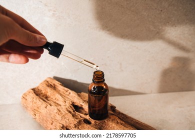 Open Amber Bottle Of Serum Close-up On Wooden Podium. A Glass Bottle With A Pipette Held By A Woman's Hand