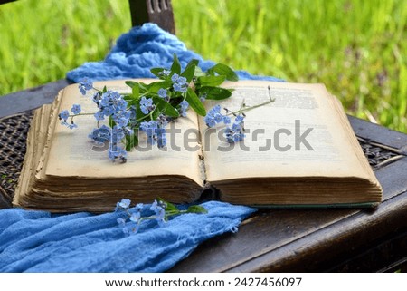An open ancient book with disheveled pages, the text is not readable, there is a bouquet of blue forget-me-nots on the book, background, knowledge, wisdom, intelligence, reading books.