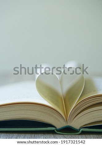 Open ancient book, two pages in the middle of the book rolled into a love heart shape, bokeh background, vertical picture with copy space