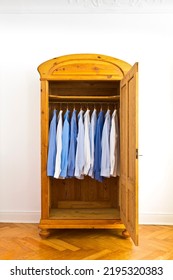 Open Antique Wardrobe With Blue Dress Shirts, Against The White Wall Of An Old Building With Parquet Flooring And Stucco Plastering, Copy Space.