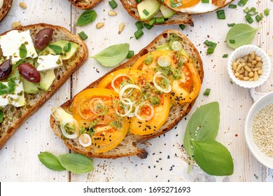 Open Avocado Sandwich Made Of Slice Of Traditional Sourdough Bread With The Addition Of Yellow Tomato, Green Pesto And Sliced Onion View From Above