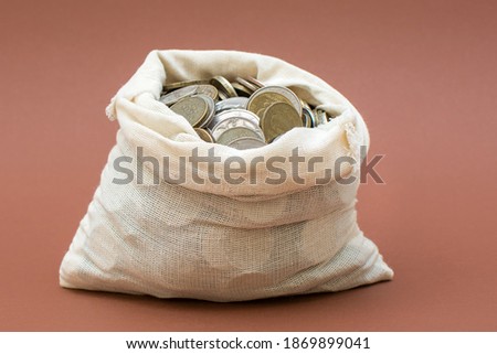 an open bag with coins stands on a beautiful brown background. Concept - deposit, savings, investment, cash, treasure, gift, charity. Horizontal photo.