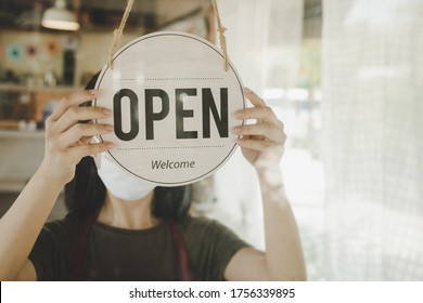 Open. barista, waitress woman wearing protection face mask turning open sign board on glass door in modern cafe coffee shop, cafe restaurant, retail store, small business owner, food and drink concept - Shutterstock ID 1756339895