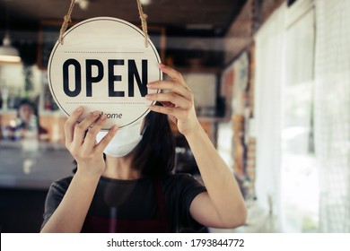 Open. Barista, Waitress Woman Wearing Protection Face Mask Turning Open Sign Board On Glass Door In Modern Cafe Coffee Shop, Cafe Restaurant, Retail Store, Small Business Owner, Food And Drink Concept