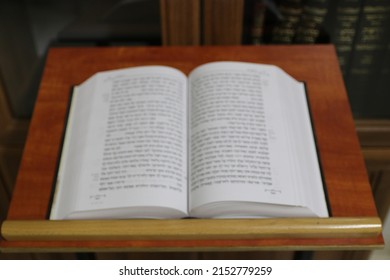 An open Bible book on a stand and a bookcase in the background