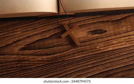 Open Bible book and wooden Christian cross on a string, wooden table