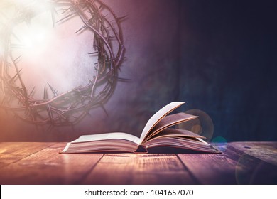 Open Bible With A Light Coming From Above On A Wooden Desk And A Crown Of Thorns In The Wall.