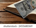 Open Bible with money on wooden table, closeup