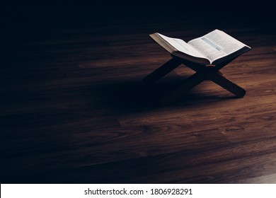 open bible on a book stand on a black background with a wooden floor and soft light