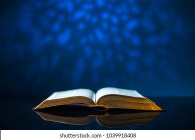 Open Bible On A Glass Desk With A Blue Background. 