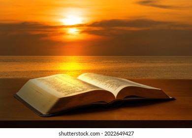 日没の光と海の背景に黒いテーブルに聖書を開く