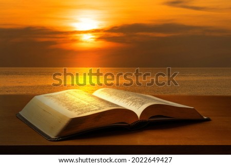 Open Bible on a table with sunset light and sea background