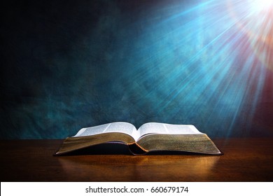 Открытая Библия на деревянном столе с светом, исходящим сверху.