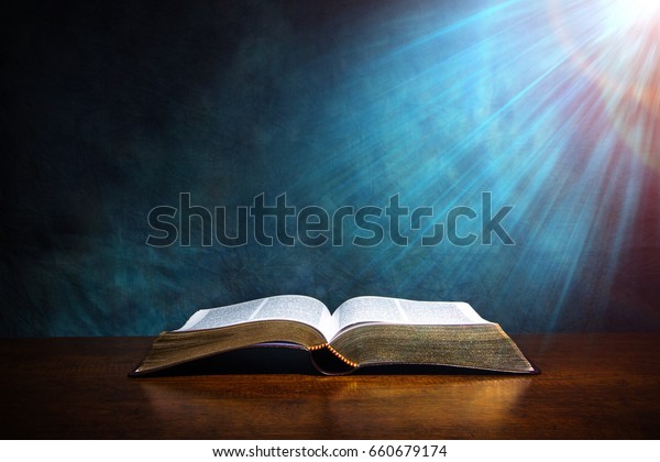 Open Bible on a wood table with light coming\
from above. ( Church concept.\
)