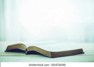 open bible on wooden table with window light