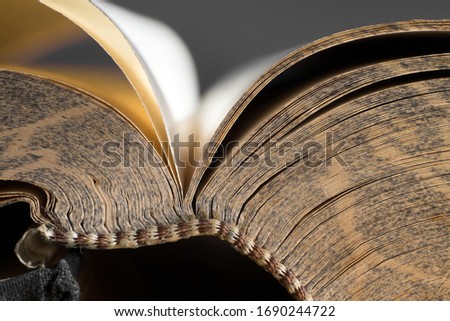 Open bible with a pattern in the edge of the pages with gold-like atmosphere and stitched or sewn binding. Black background, narrow depth of field